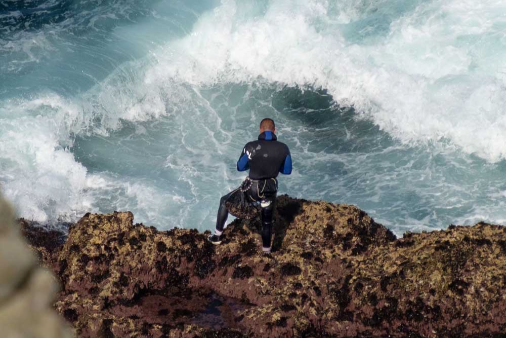 A coasteerer on the rocks watching heavy surf, on an Anglesey Adventures session