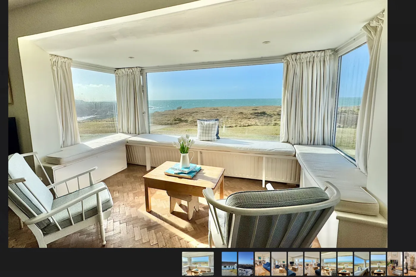 A property gallery open in a lightbox: a bay window looking out to sea, with a strip of thumbnails beneath